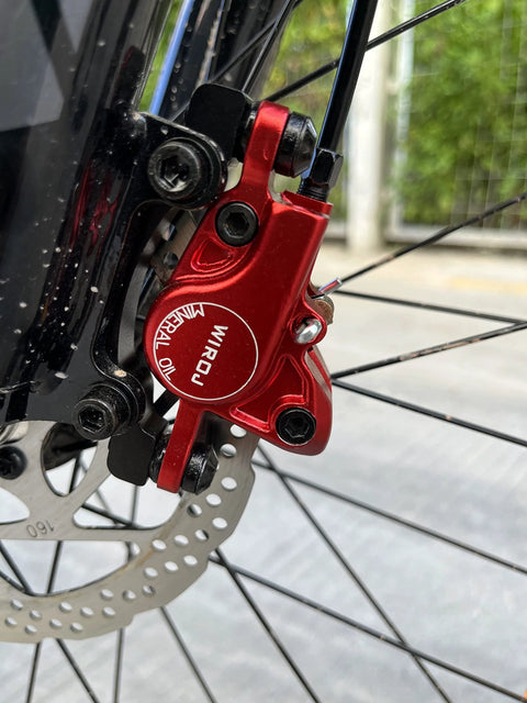 Red WIROJ hydraulic disc brake caliper, side view, mounted on front MTB fork with drilled rotor