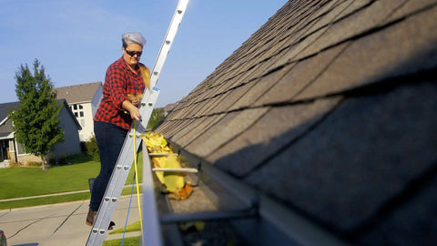 Person cleaning gutters on a ladder with debris on a residential roof.