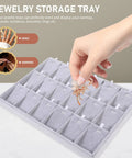 Hand placing a decorative earring in the Super Smooth Large 18 Compartment Velvet Jewelry Storage Tray With Handy Necklace And Watch Display Pad Totally Organized For Craft Sessions And Stylish Desk Vibes.
