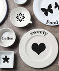 Set of four white ceramic dinnerware pieces with black laser-engraved decals (heart, flowers, butterflies).