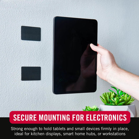 Velcro Brand heavy-duty 4x2 in adhesive mounting strips, black; two strips on wall beside a tablet.