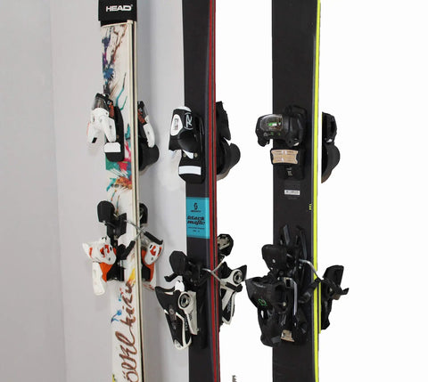 Badass Five Pack Ski Wall Hangers securely grip multiple ski boards with varying bindings in a garage setup.
