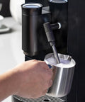 Game Changer Automatic Espresso Machine Packing Built In Milk Frother in action, frothing milk with steel pitcher.
