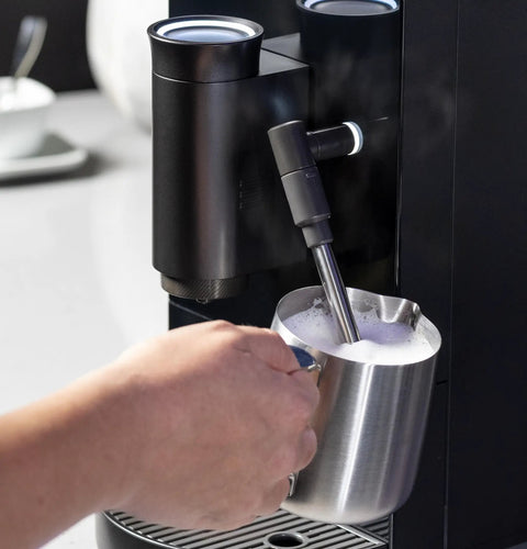 Game Changer Automatic Espresso Machine Packing Built In Milk Frother in action, frothing milk with steel pitcher.