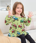 Ultra Soft Cotton Baby Girl Blouse With Ruffled Sleeves Featuring Farm Tractor Print On Green Background For Everyday, Holidays And School, Cozy Long Sleeve Top, Machine Washable, Easy Care 5T worn by a girl sitting on a sofa.