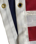 Close-up of Outdoor 3x5 Ft American Flag Deluxe Heavy Duty Spun Polyester with brass grommets and label detailing washing instructions.