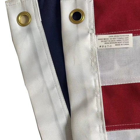 Close-up of Outdoor 3x5 Ft American Flag Deluxe Heavy Duty Spun Polyester with brass grommets and label detailing washing instructions.