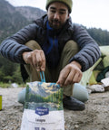 Camper using BPA free folding utensil on camping trip with mountain scenery.