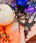 Hand holding EZGrip 25 Ft Heavy Duty Outdoor Extension Cord With Multiple Outlets among Halloween lights and a white pumpkin.