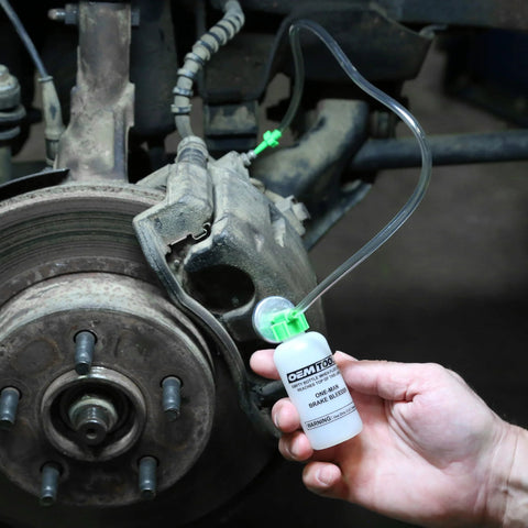 OEMTOOLS Bleed-O-Matic brake bleeder kit with white opaque bottle and clear hoses connected to a vehicle brake caliper