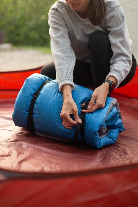 Two Pack 48 Inch Sleeping Bag Straps With Quick Release Buckles For Universal Fit securing blue sleeping bag outdoors.