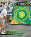 Man practicing golf with Ultra Large 70x70 Inch Golf Chipping Net and turf mat in garage for backyard practice.