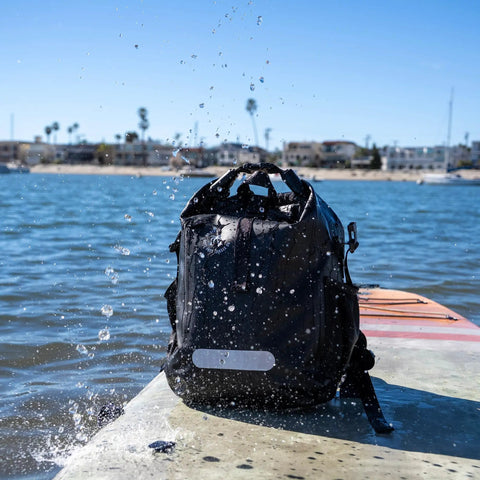 25L Waterproof Surf Backpack For Adventure With Roll Top Closure Keeps Gear Dry In Any Weather on a wet dock by the beach