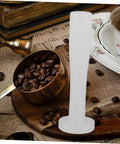 Plastic Espresso Tamper For Home And Commercial Coffee Making No Frills Durable Press Tool on wooden table with coffee beans.