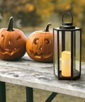Outdoor Solar Powered Lantern With Flameless Candle 18 Inch Black Metal And Glass Waterproof Hanging Tapered Candle Lamp next to pumpkins