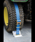 Heavy Duty E Track Wheel Chock Tie Down Kit with blue ratchet strap securing a tractor tire for safe ATV hauling.