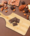 Bamboo charcuterie board with handle, 11 x 5 inches, natural finish; chocolate pieces on top.