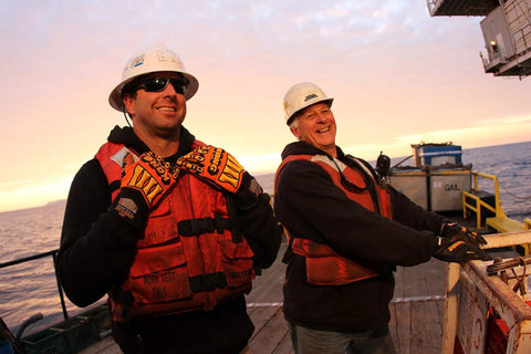 Two workers on an oil rig wearing KONG SDX2 05 XL Oil And Gas Safety Impact Gloves Orange Heavy Duty Work Gloves at sunset.