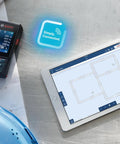 Beast Of A Blaze Outdoor Connected Laser Measure with 400 ft range displayed next to a tablet showing floor plans on a worksite table.