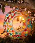 6 Inch Glass Mosaic Hanging Bird Feeder For Outdoors With Fly Through Opening showing colorful confetti pattern at sunset