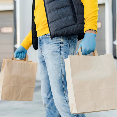 Person wearing Heavy Duty Textured Nitrile Disposable Gloves Blue Medium 3.5 Mil carrying brown paper bags.
