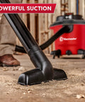 Heavy Duty 12 Gal Wet Dry Shop Vac With Beastly 5.5 Peak HP Motor And Nine Must Have Cleaning Attachments For Cranking Nasty Garage Jobs And Spills Features Classic Red Plastic Design, close-up of black nozzle on dusty floor.