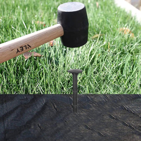 80 Pack Plastic Lawn Stakes Six Inch Ground Anchors Spikes Heavy Duty being hammered into weed fabric in a garden setup