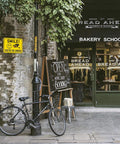 Bakery storefront with bike and Two Pack Smile Youre On Camera Sign For Outdoor Video Surveillance Signs UV Printed Aluminum visible on wall.