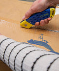 Person using 2-In-1 Folding Jab Saw With Retractable Utility Knife For Quick Drywall Cuts on cardboard box