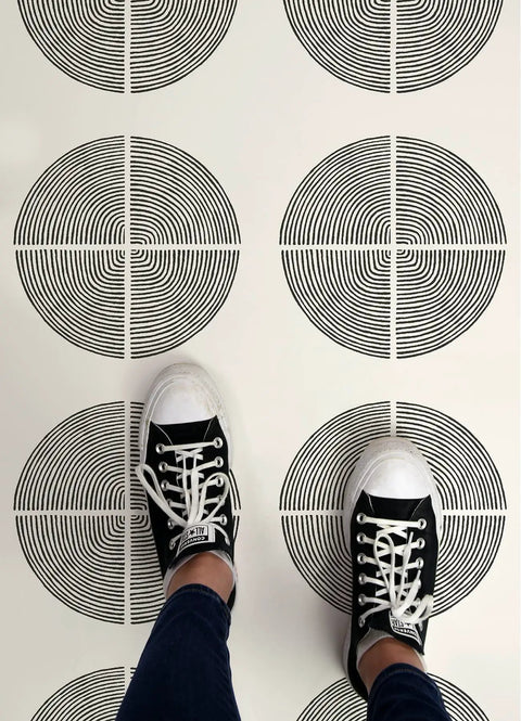 Black and White Luminary Peel and Stick Vinyl Floor Tiles 12x12 with circular pattern, person standing on tiles, Mid Century style
