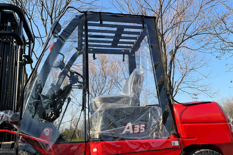 All Weather Forklift Cab Enclosure Cover With Heavy Duty UV Protection And Waterproof Vinyl Universal Fit For Forklifts Up To 6000 Lb Easy Zip Access Keeps Cold Air Rain Snow Out. Image showing a transparent cab cover fitted on a red forklift.
