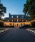Outdoor String Lights 200 Ft Connectable G40 LED Bulbs adorn a large house, creating a cozy vibe alongside a driveway at dusk.