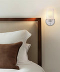 Kira Home Phoebe 8" Modern Industrial Wall Sconce for Bathroom Vanity, Pack of 2 mounted beside a bed, chrome finish with frosted glass.