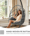 Woman sitting in Chill Outdoor Hanging Egg Chair With Stand For Patio And Garden, Cushioned Wicker Rattan Swing Chair Up To 300 Lbs, Perfect For Balcony Or Bedroom, Gray, in a sunlit room.