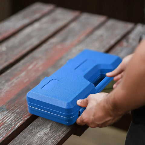Man holding blue case of Beefy 6 Ton Manual Knockout Hole Punch Kit With Ratchet Wrench And Six Die Set on wooden table