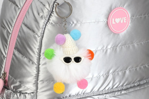 Close-up of a silver backpack with a colorful pompom keychain and love badge. 17 Inch Water Resistant Wheeled Laptop Backpack With Convertible Rolling Bag Design Full Size Laptop Compartment TSA Friendly Lightweight Travel And College Bag For Men Women Adults Overnight Trips Beautiful Silver.