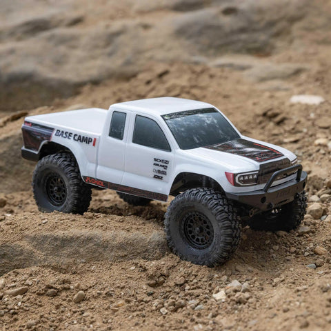SCX24 Base Camp 4x4 Rock Crawler Ready To Run RC Truck on rocky terrain, 1/24 scale, white body, thick tires, detailed grille