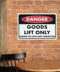 Danger sign 'Goods Lift Only' mounted on a brick wall near a wooden table.