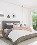 Bright bedroom with grey bed, white linens, pink throw, pendant lights, nightstand, framed art, and open window to greenery