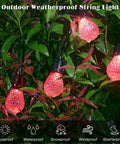 Outdoor weatherproof string lights with red bulbs hanging among leafy green plants, showcasing sunproof and waterproof features.