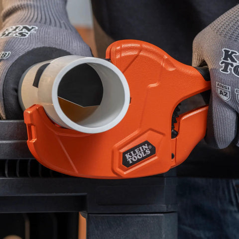 Ratcheting PVC Pipe Cutter For 2 Inch ID Pipes And 2 3 Eighths Inch OD, One Handed Operation, Lightweight Soft Grip Handles, Replaceable Blades, Cuts Schedule 40 And 80 PVC CPVC And PEX. Orange ratcheting PVC pipe cutter gripping 2-inch plastic pipe