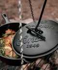 Heavy Duty Dutch Oven Lid Lifter With Coil Handle lifting black lid on grill with rosemary and lemon slices