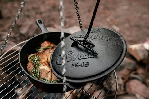 Heavy Duty Dutch Oven Lid Lifter With Coil Handle lifting black lid on grill with rosemary and lemon slices