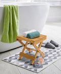 Foldable Shower Stool For Tiny Bathrooms Bamboo Foot Rest And Shaving Stool beside bathtub on bathroom rug.