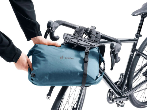 Person mounting 14 Liter Waterproof Handlebar Mounted Bike Bag With Reflective Details And Gear Loops on bike handlebars.