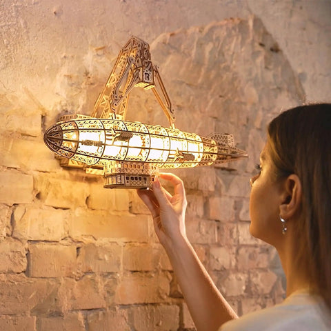Person interacting with Luminous Zeppelin LED 3D Wooden Puzzle Kit For Adults, mounted on a brick wall, lit up as a warm lantern