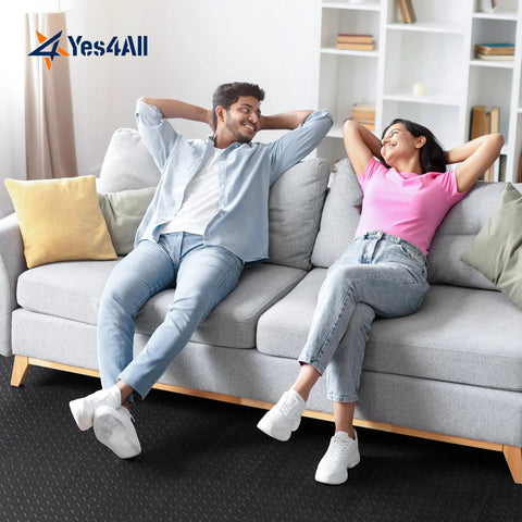 Two people sitting on a sofa over interlocking foam floor tiles 24x24 puzzle mats with border, black color, in a living room.