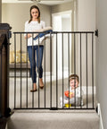 Extra Tall Baby Gate For Stairs And Doorways Walk Through With Door Hardware Mounted Gate For Babies Toddlers And Pets Expands From 24 To 40.5 Inches 36 Inch Tall Black installed at top of stairs with child and adult nearby.