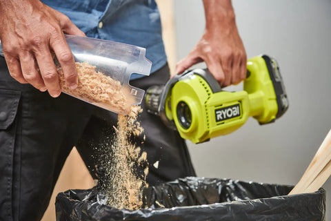Person pouring wood shavings from clear container into trash with Compact 18V Lithium Ion Handheld Vacuum With Beast Mode Suction Power.