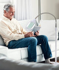 Man using LightView Pro LED Magnifying Floor Lamp with Full Page Glass Lens, Daylight Full Spectrum Light, reading on a sofa.